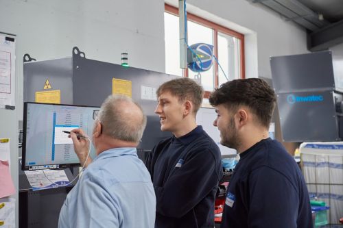 Älterer Mitarbeiter erklärt den beiden Azubis etwas an einem Touch-Screen