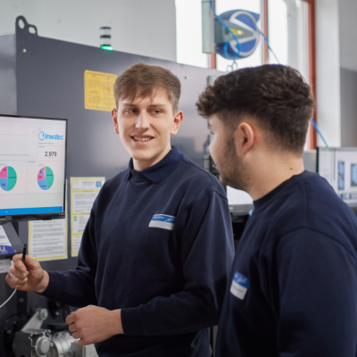 Zwei Auszubildende unterhalten sich vor der Sortieranlage für getragene Berufsbekleidung.