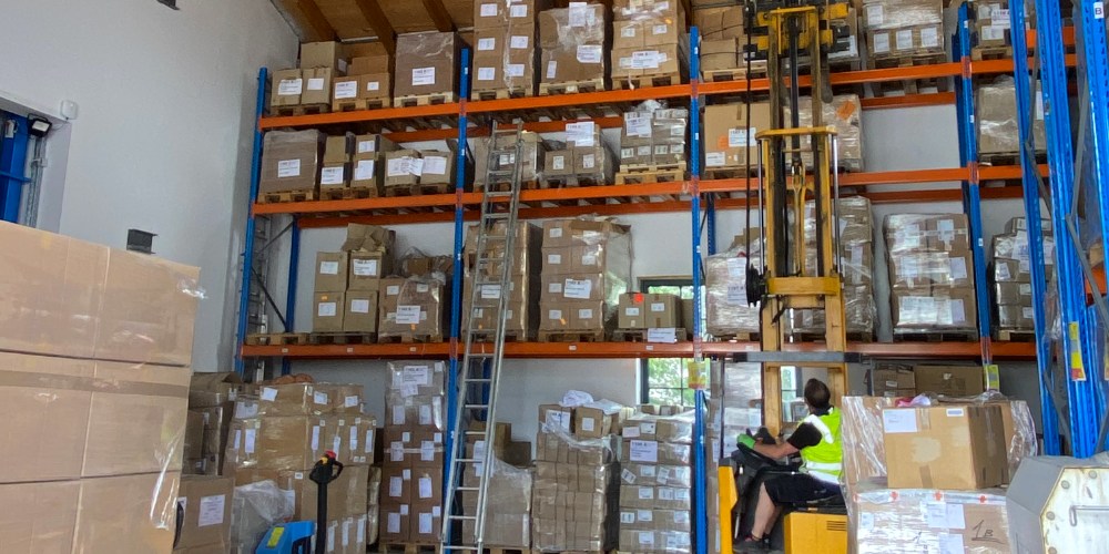 Hausmeister lagert mit einem Stapler einen Karton Mietwäsche aus einem Hochregal in dem Wäschelager aus